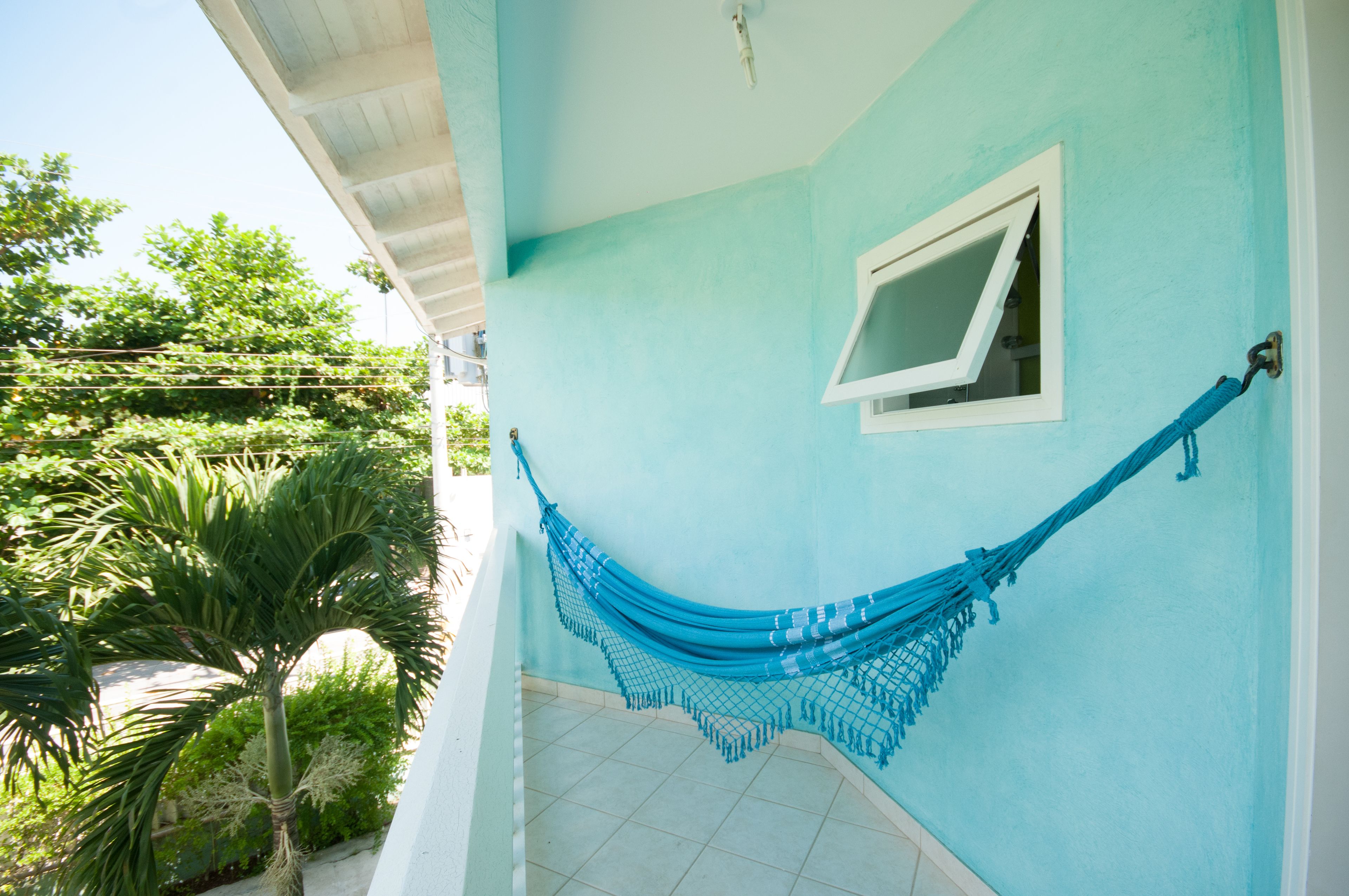 A room with a hammock hanging on the wall, a window, and a view of greenery outside.