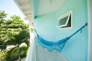 Una habitación con una hamaca colgada en la pared, una ventana y vistas al verde exterior.