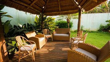 A covered outdoor seating area with wicker furniture and a thatched roof.