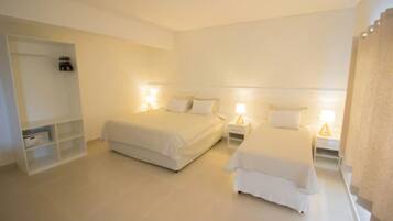 Una habitación de hotel con dos camas, un armario blanco y una mesita de noche con lámpara.
