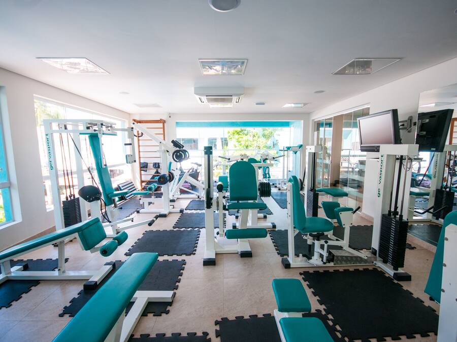 Een sportschool met diverse fitnessapparatuur, grote ramen en uitzicht op groen.