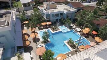 A rooftop pool with multiple levels, surrounded by palm trees and umbrellas, indicating a resort setting.