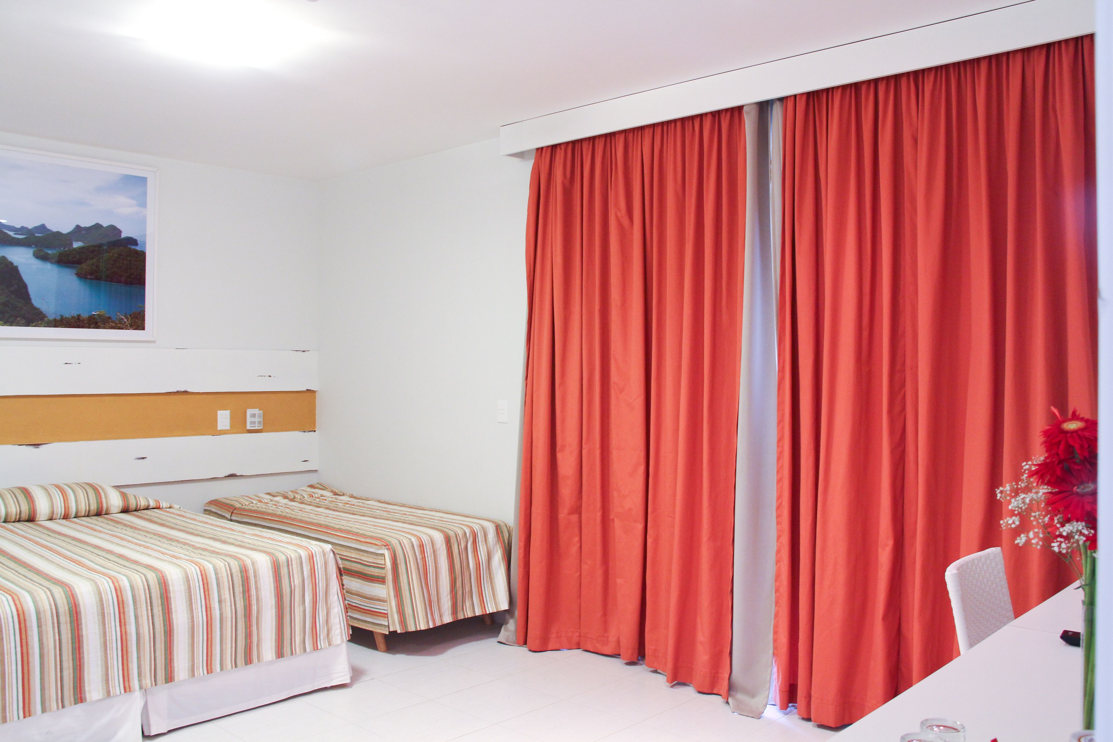 A hotel room with two beds, a large window with a view of a coastal landscape, and a desk with a chair.