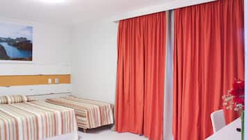 A hotel room with two beds, a large window with a view of a coastal landscape, and a desk with a chair.