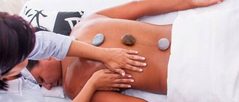 A massage therapy session with a person lying face down, receiving pressure on the back with stones.