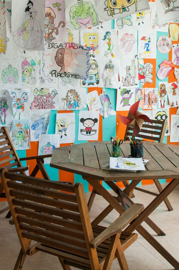 Una habitación con una mesa de madera, sillas y una pared decorada con dibujos y obras de arte infantiles.