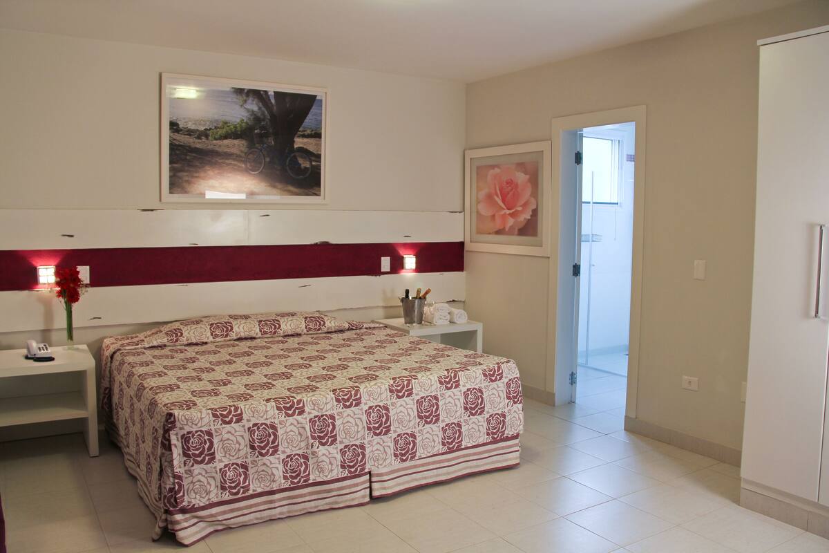 Ein Schlafzimmer mit einem Bett, Nachttischen, einem Beistelltisch und einem gerahmten Bild an der Wand.