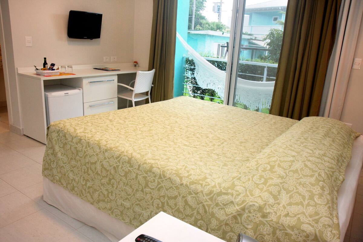 Ein Hotelzimmer mit einem Bett, einem Schreibtisch, einem Stuhl, einem Kühlschrank und einem Fernseher an der Wand.