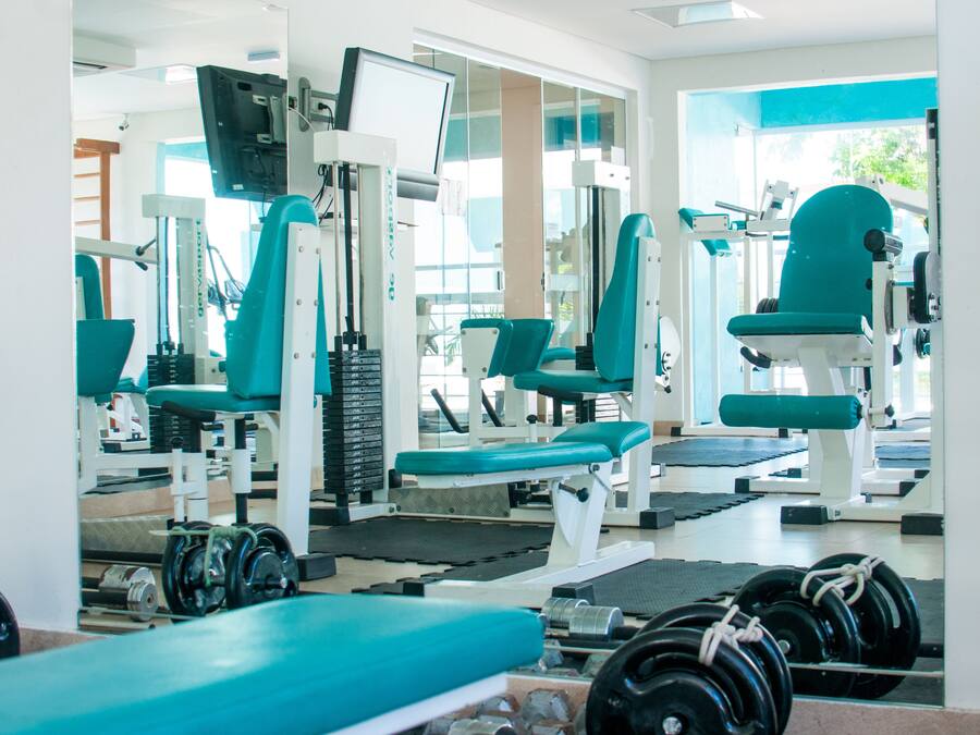 Uma academia com diversos equipamentos de exercício e pesos livres.