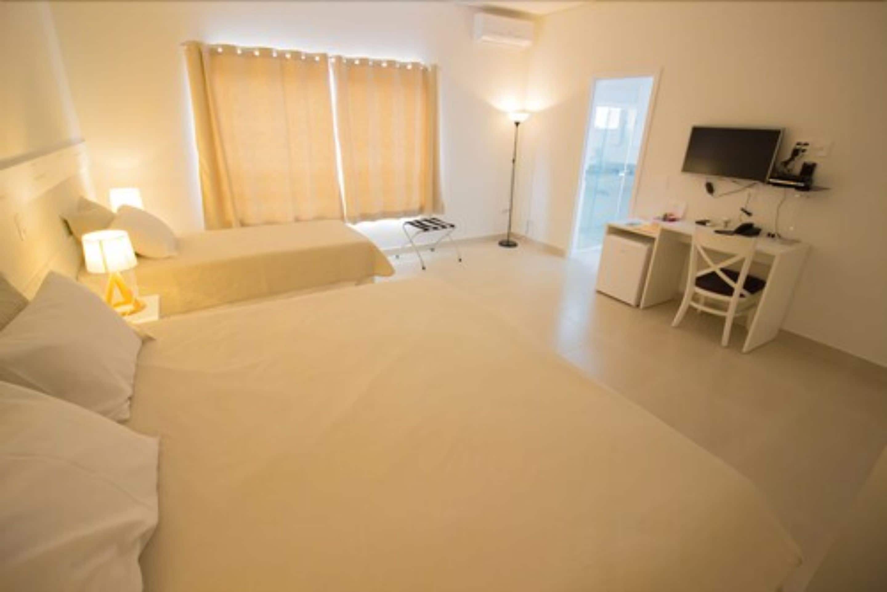 A hotel room with a bed, bedside table, lamp, desk, chair, and a television.