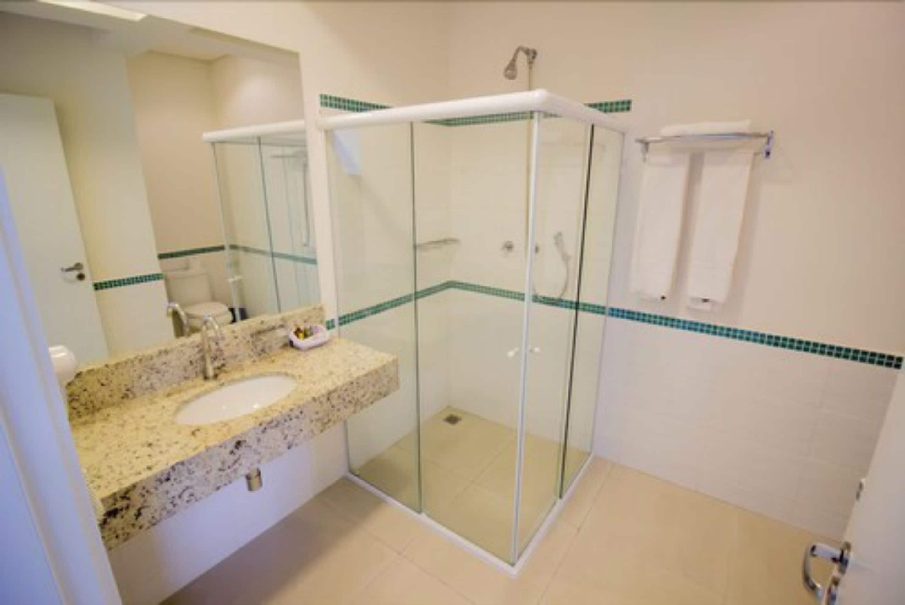 A bathroom with a glass-enclosed shower, a granite countertop sink, and a mirror.