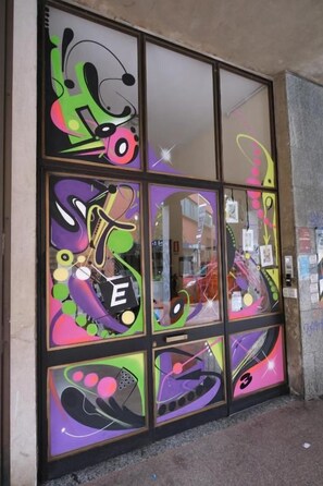 A storefront with large windows featuring colorful abstract designs. - Hostel 3 (Milan)