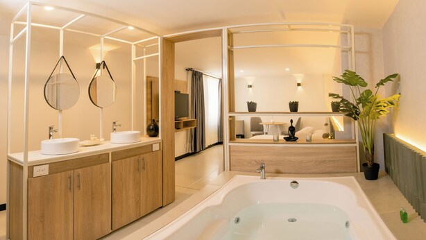 A modern bathroom with a freestanding bathtub, wooden cabinets, a vanity with a mirror, and a potted plant. - Hotel Príncipe (Tulua)