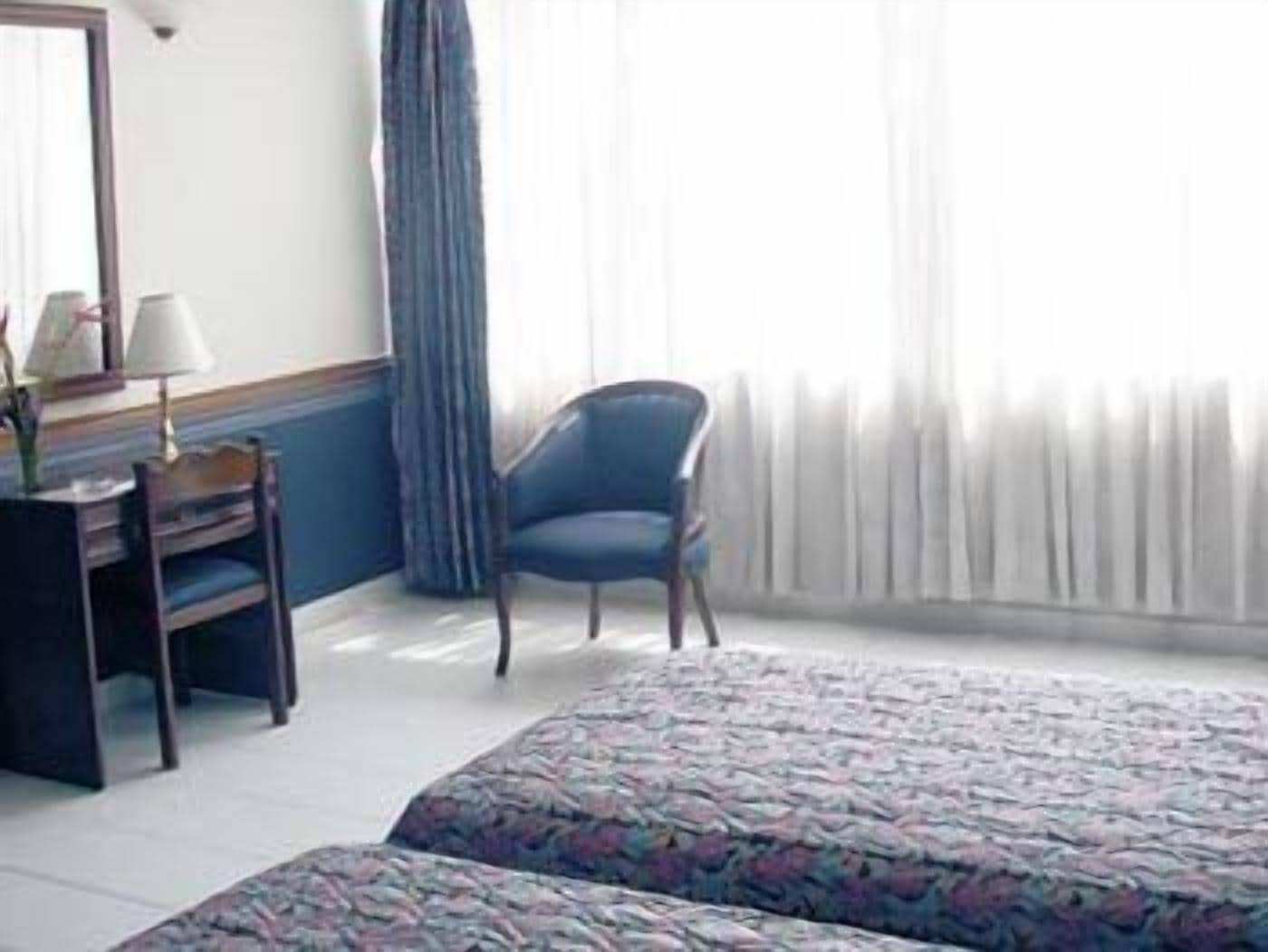Une chambre d’hôtel avec un lit, un bureau avec une lampe, une chaise et une fenêtre avec des rideaux.