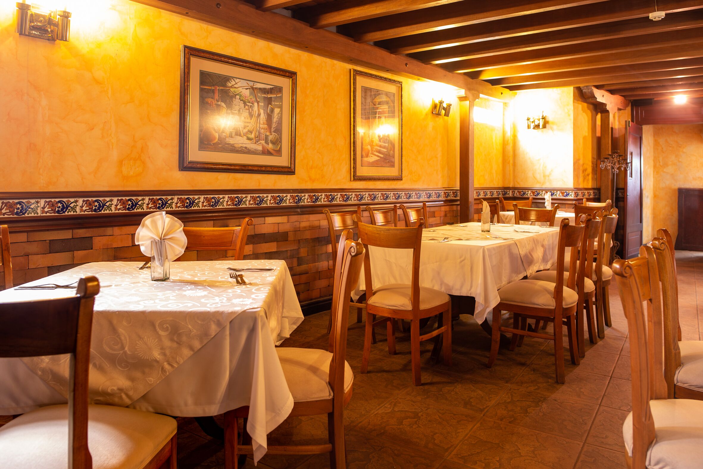 Un restaurante con varias mesas y sillas, obras de arte enmarcadas en las paredes y suelo de baldosas.