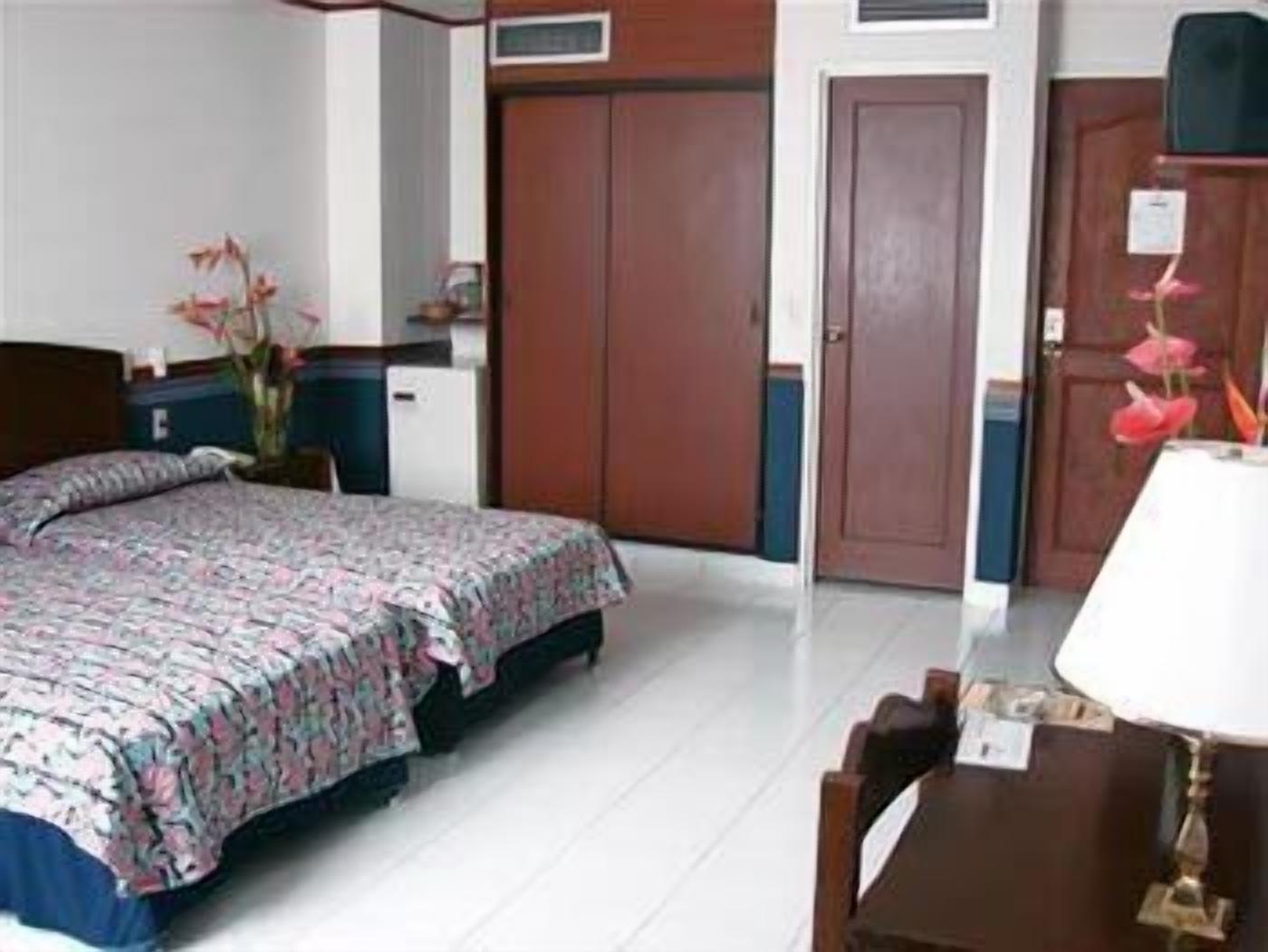 Habitación de hotel con cama, escritorio, silla, armario y una pequeña mesa con lámpara.