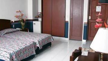 Habitación de hotel con cama, escritorio, silla, armario y una pequeña mesa con lámpara.