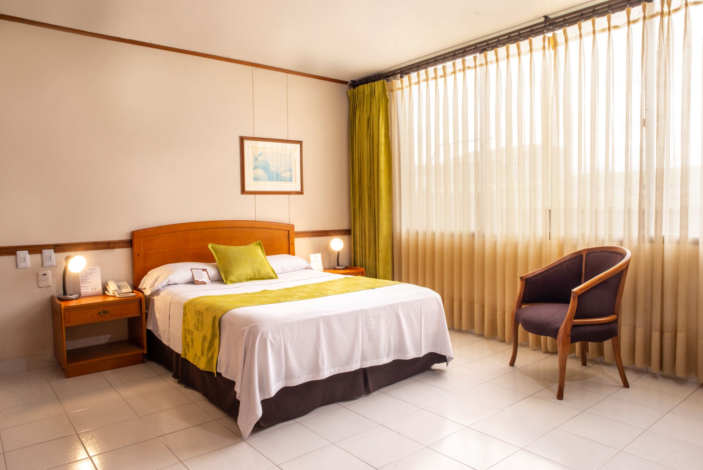 Una habitación de hotel con una cama, una silla, una mesita de noche y una ventana con cortinas.