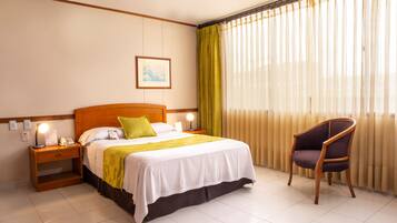 Una habitación de hotel con una cama, una silla, una mesita de noche y una ventana con cortinas.