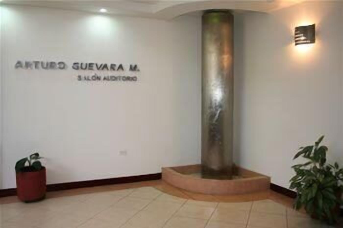 Un área de recepción con un pilar, una planta en maceta y un cartel en la pared.