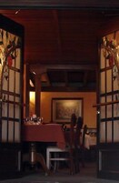 A dining area with a table set for two, a painting on the wall, and a wooden ceiling.