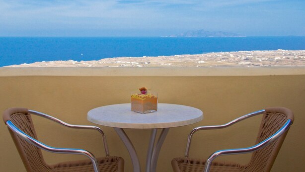 Una mesa redonda con un pastel y dos sillas de mimbre orientadas hacia una playa con vistas despejadas al mar y a la costa lejana.