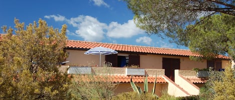 Un bâtiment à deux étages, avec un toit recouvert de tuiles rouges, une porte bleue et un parasol blanc au premier plan.