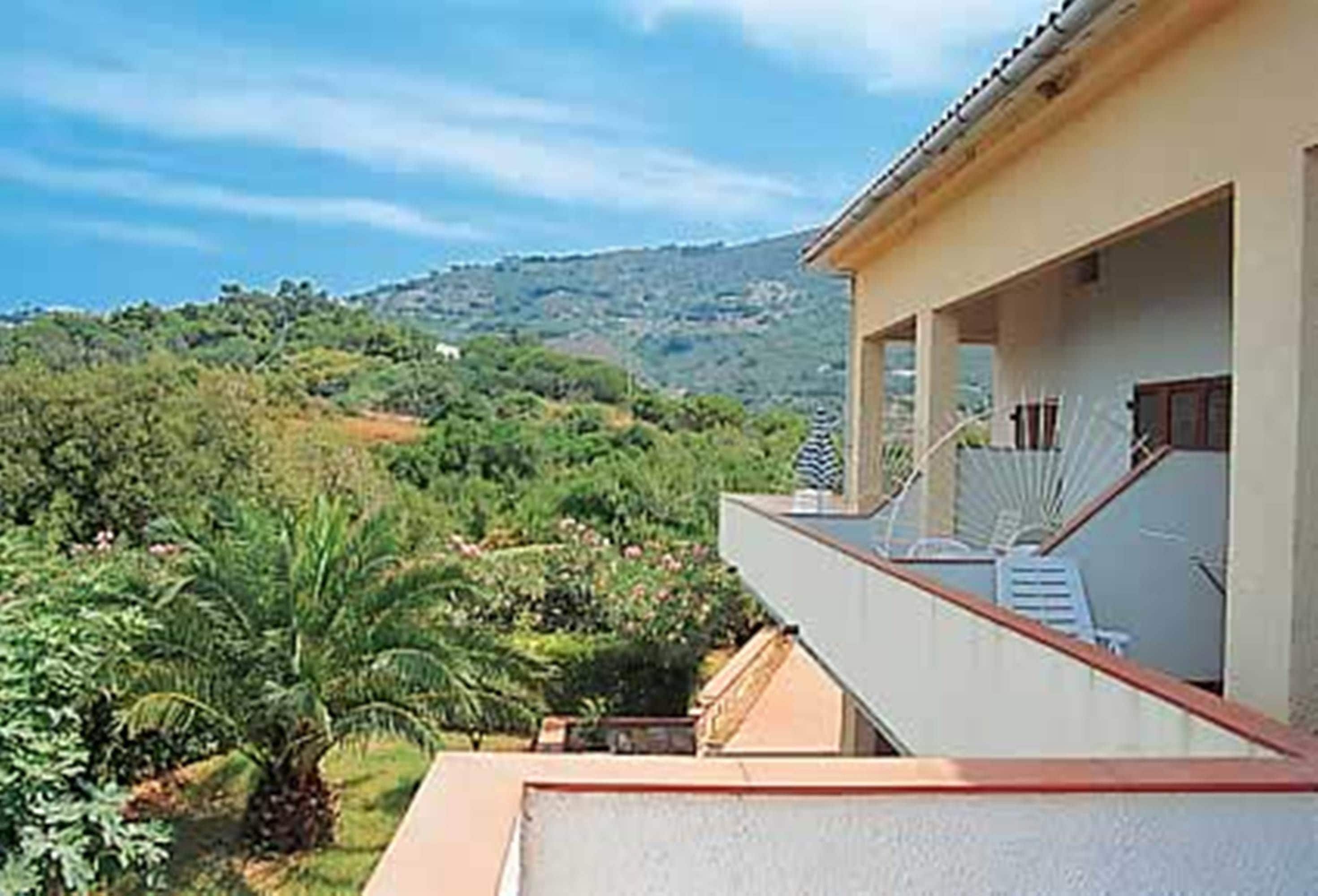 Un hotel con un balcone affacciato su un rigoglioso giardino e delle colline.