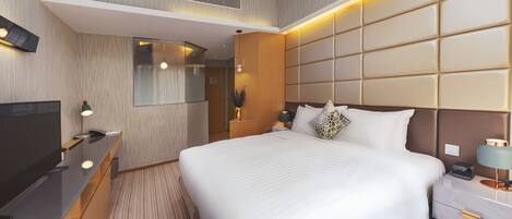 A modern hotel room with a large bed, a TV, a bedside table with a lamp, and a mirror.