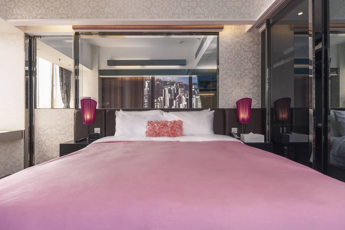 A modern hotel room with a large bed, a city view through floor-to-ceiling windows, and a minimalist design.