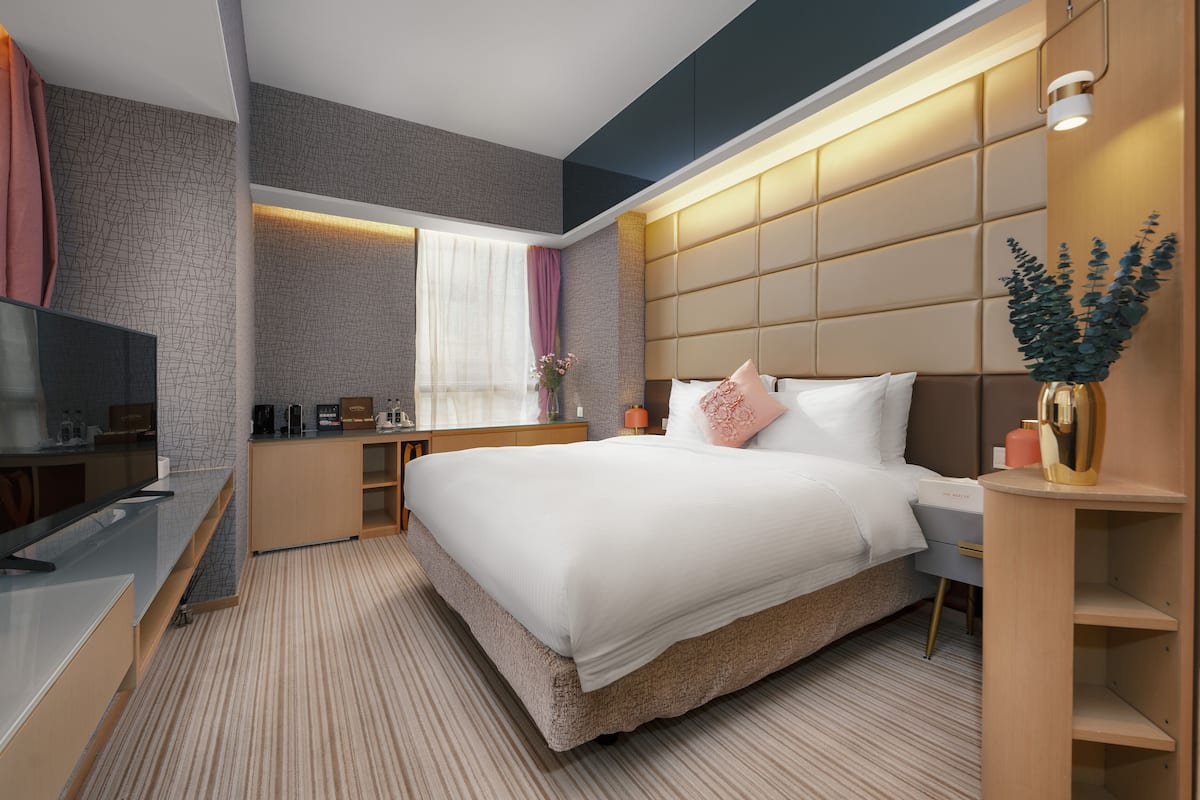 A modern hotel room with a large bed, a TV, a desk, and a window with curtains.