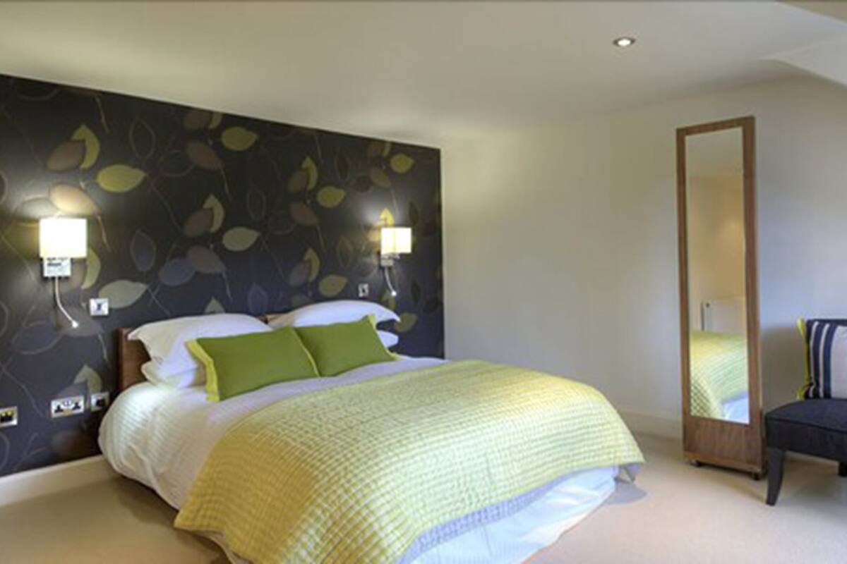 A bedroom with a bed, green pillows, a nightstand, and a wall-mounted lamp.