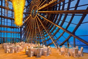 Un grand espace intérieur doté d’une structure circulaire, avec des tables dressées pour le repas et des chaises disposées autour.