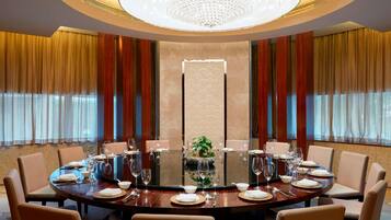 Una mesa redonda de comedor dispuesta para una comida formal, rodeada de sillas, con un candelabro sobre ella y cortinas en las ventanas.