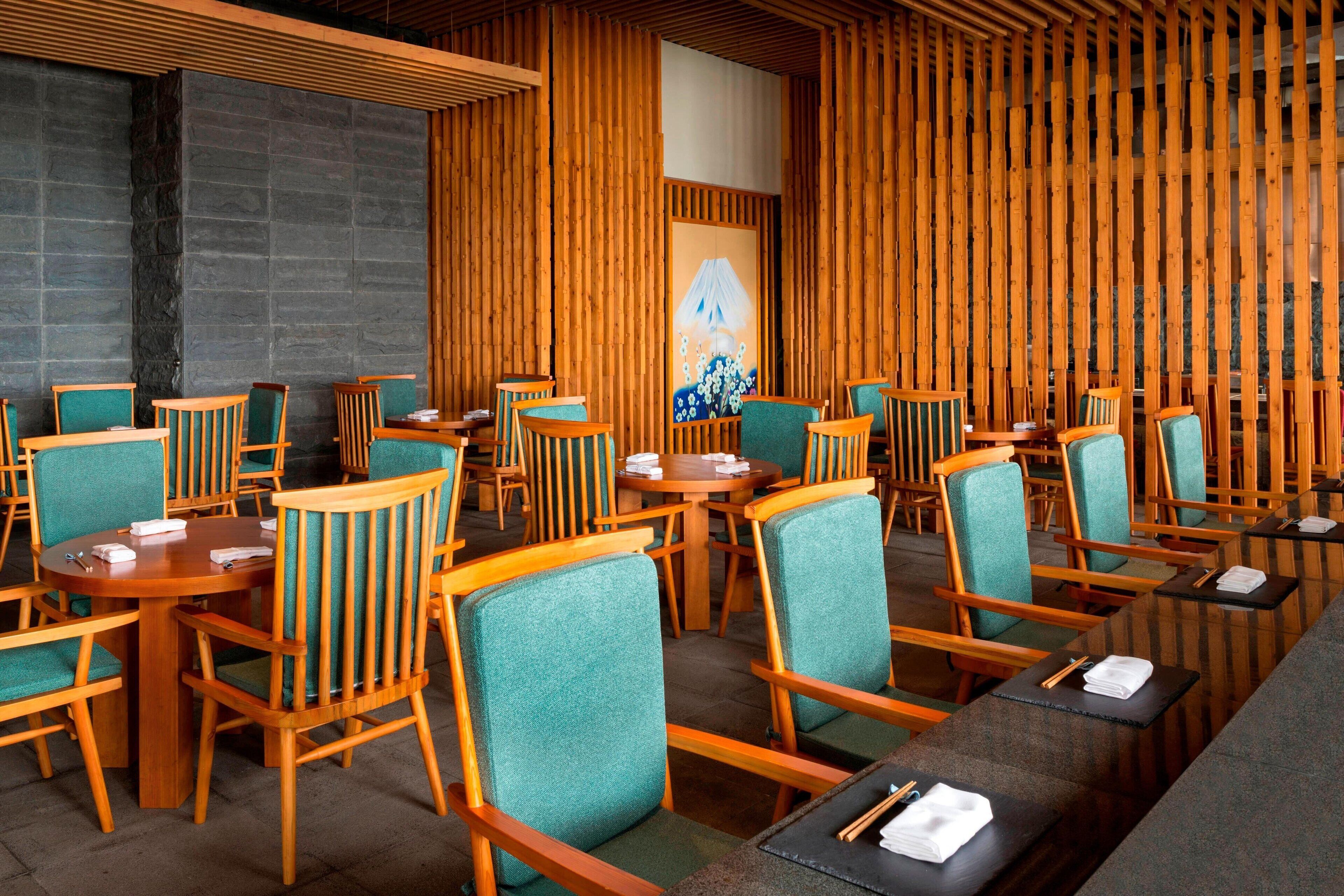 Ein Restaurant mit Holzwänden, smaragdgrünen Stühlen und runden Tischen.