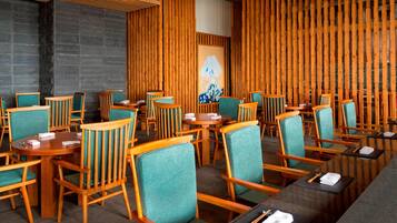 Ein Restaurant mit Holzwänden, smaragdgrünen Stühlen und runden Tischen.