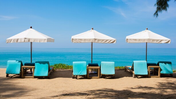 Un espacio de descanso frente al mar con sombrillas blancas y sillas reclinables color turquesa.