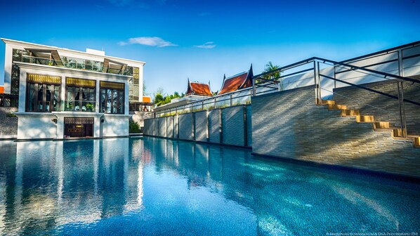 Une piscine bordée d’un bâtiment moderne doté de grandes fenêtres et d’un mur en pierre.