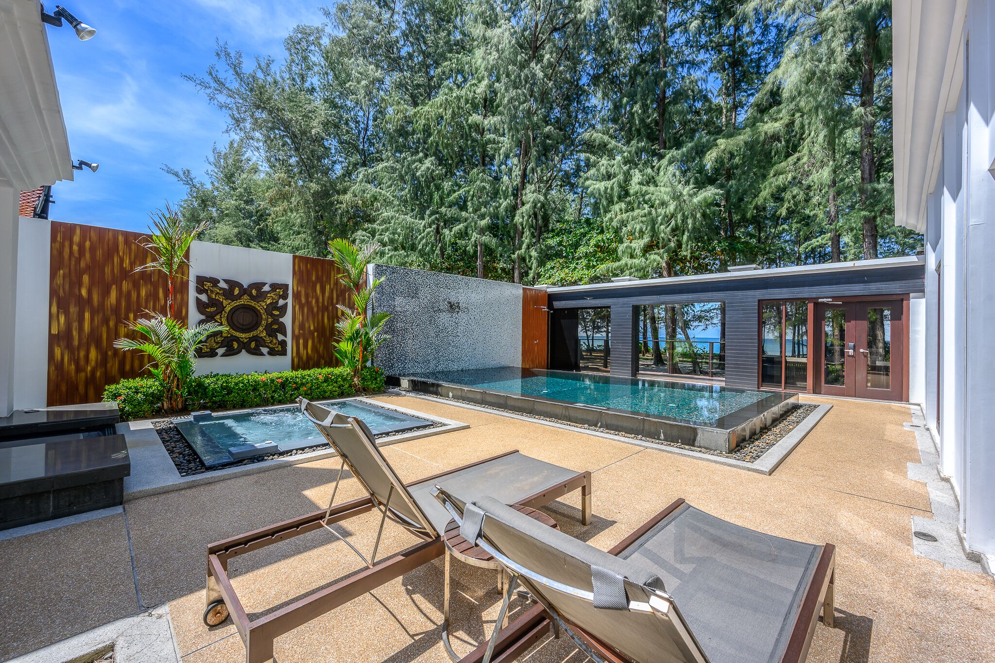 Un área de piscina moderna al aire libre con sillas de descanso, un jacuzzi y un muro de piedra.