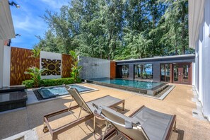 Un espace piscine extérieur moderne, doté de chaises longues, d’un jacuzzi et d’un mur en pierre.