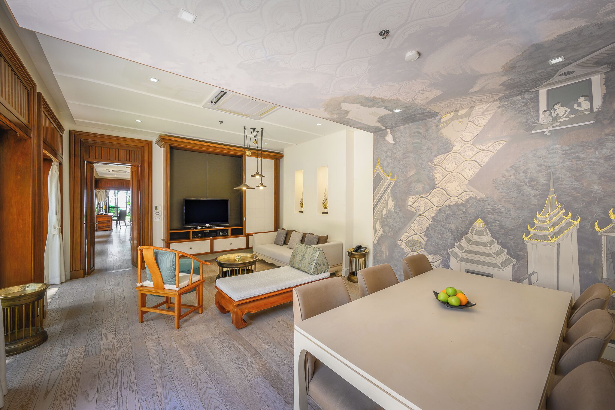 A spacious living area with a sofa, a TV, and a dining table with fruit.