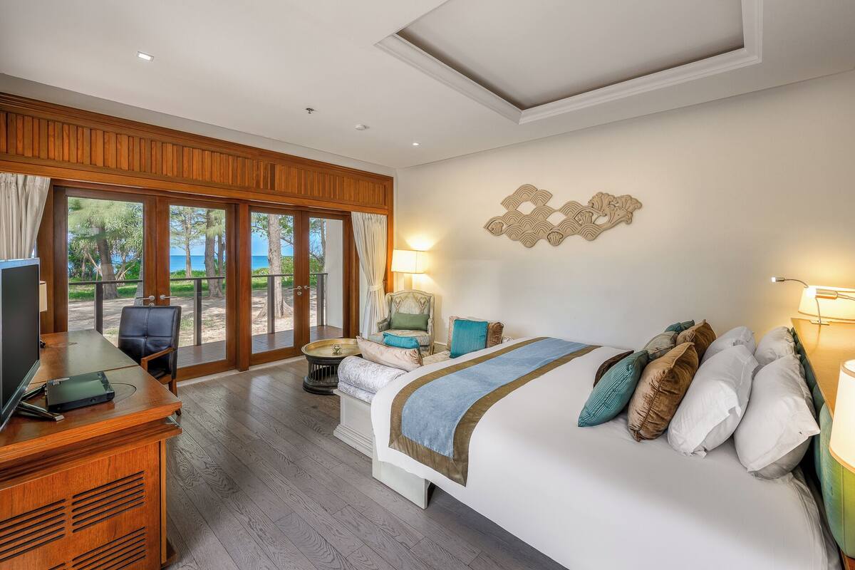 A hotel room with a bed, a desk with a computer, a chair, and a view of the outdoors.