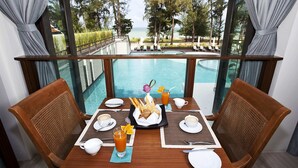 Mesa de jantar com café da manhã montado, com vista para uma piscina e para o oceano.