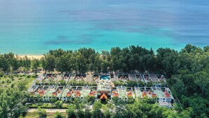Vista aérea de un resort con varias construcciones tipo bungaló, una piscina central y una playa al fondo.