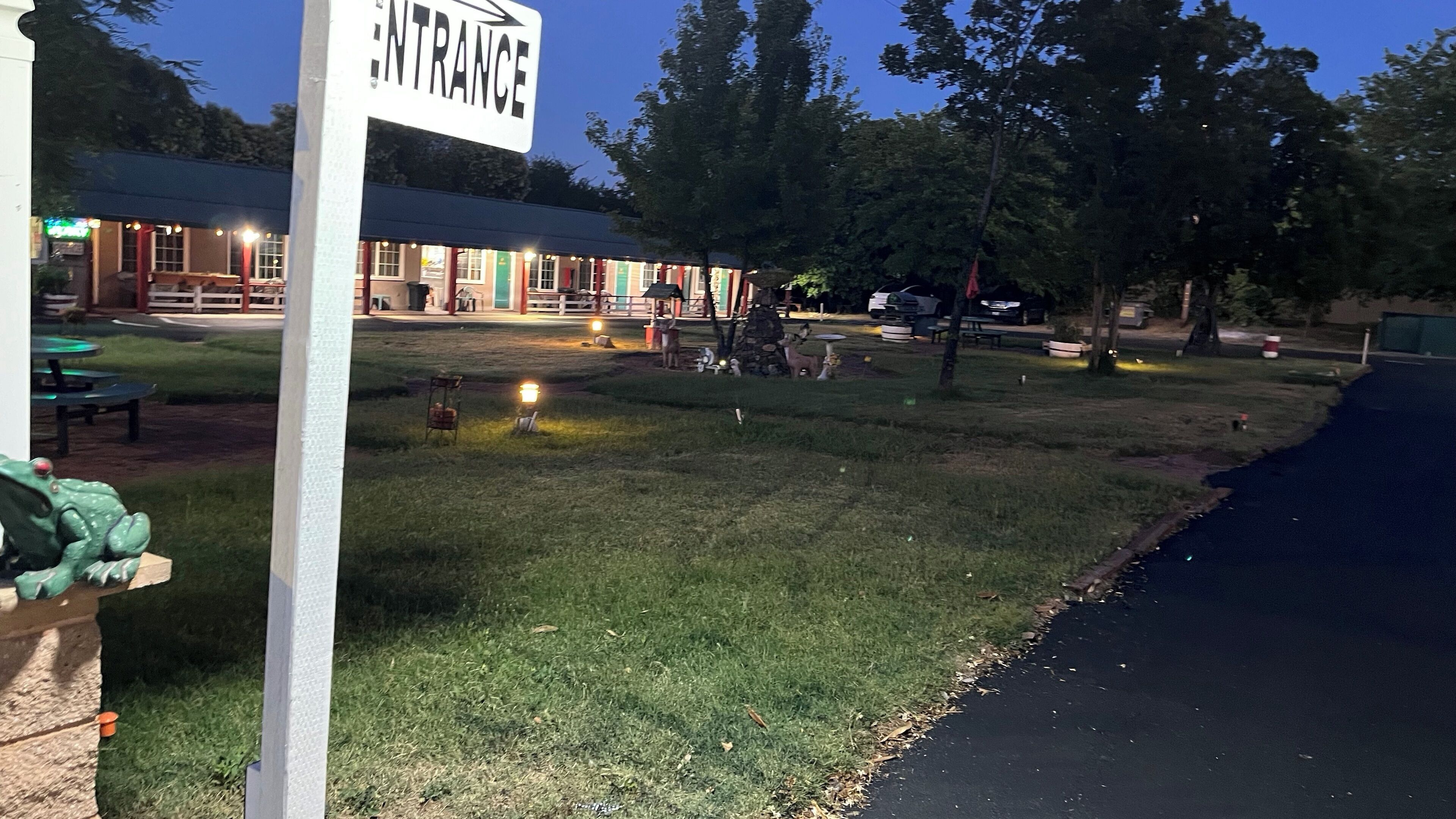An entrance sign, a building with outdoor seating, and a grassy area with trees.