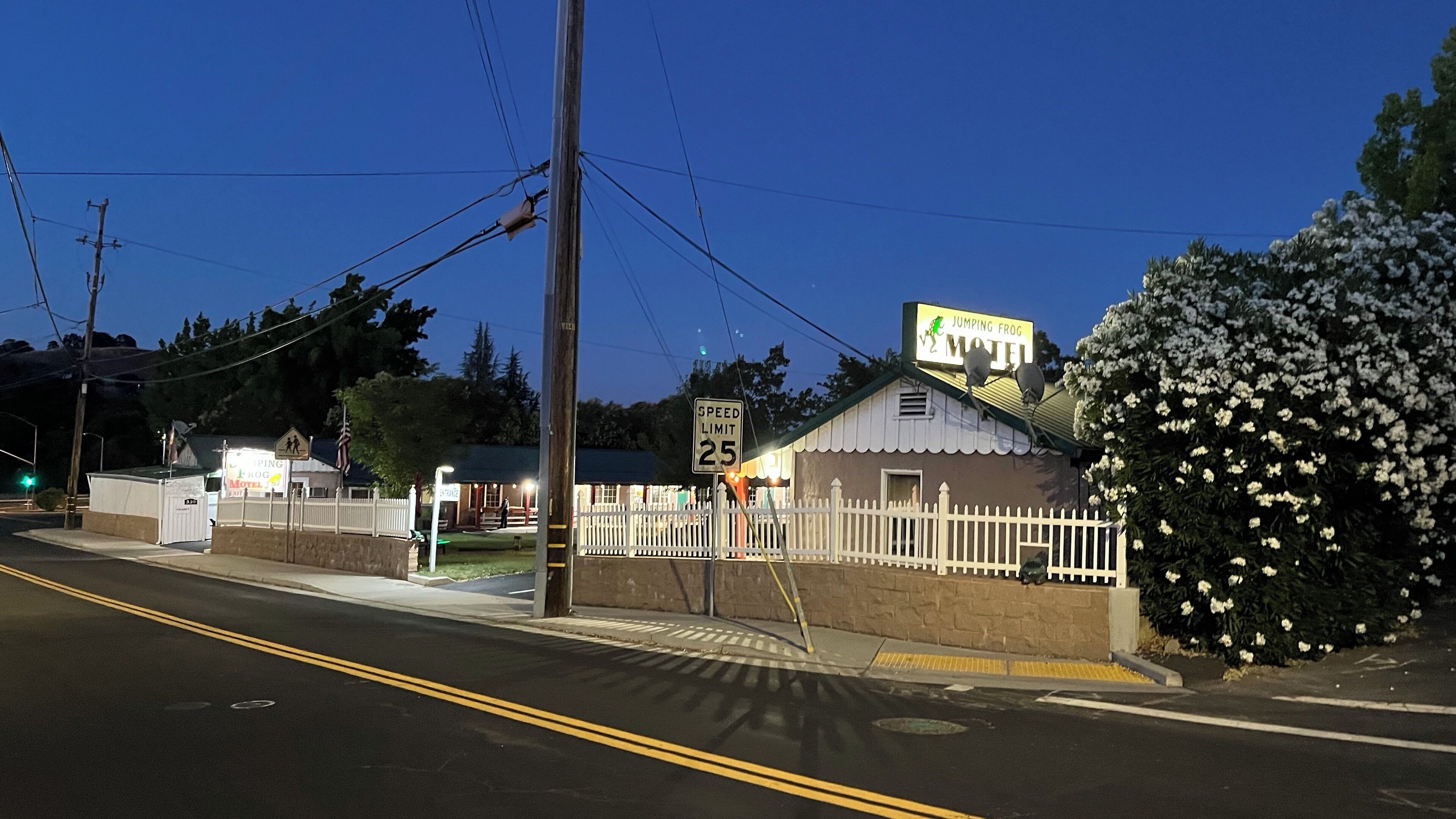 Un motel con un cartel de límite de velocidad de 25 millas por hora, una entrada cercada y un letrero que dice 'Jumping Frog Motel'.