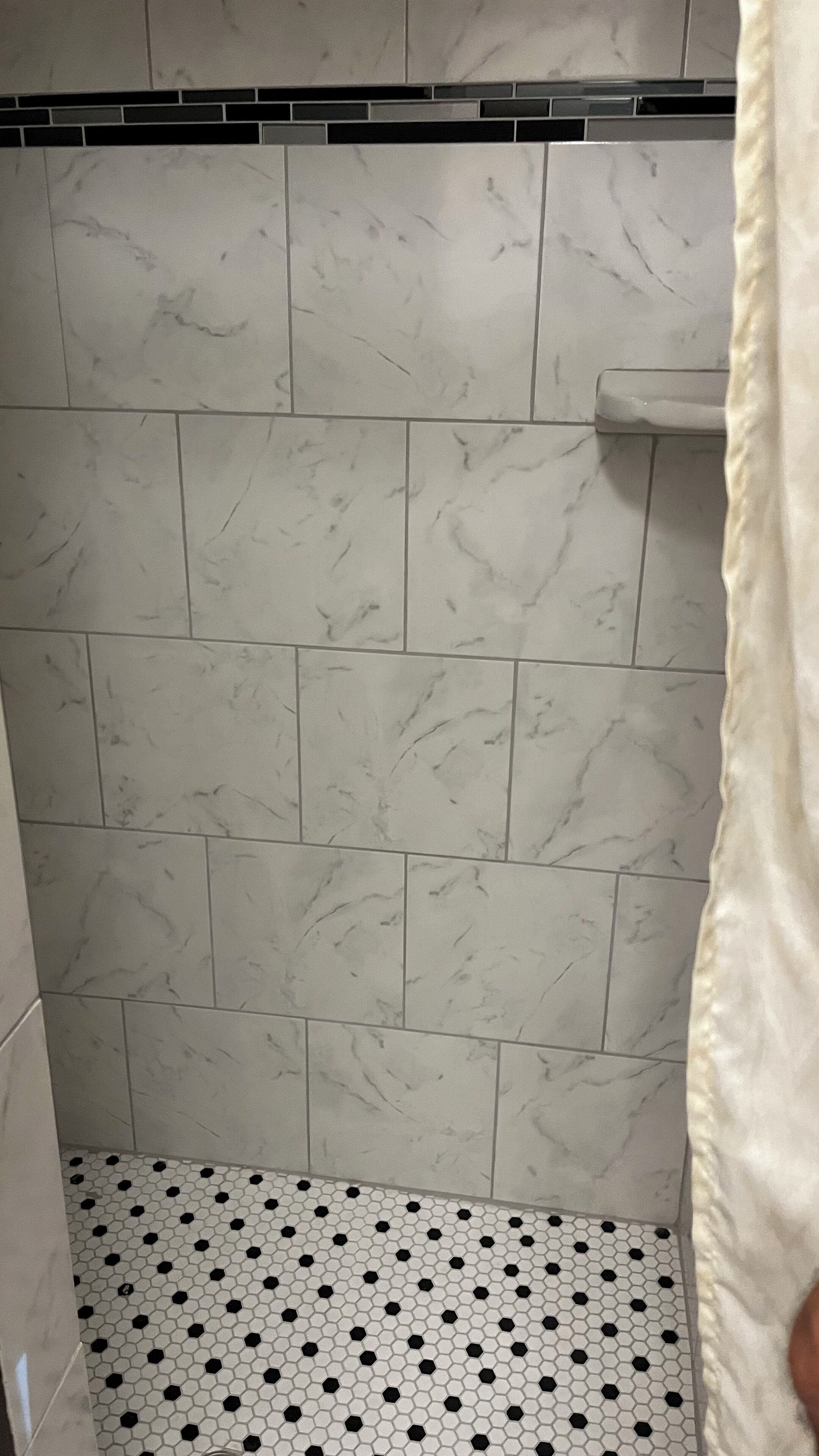 A bathroom with white marble tiles and a black and white hexagonal patterned floor.