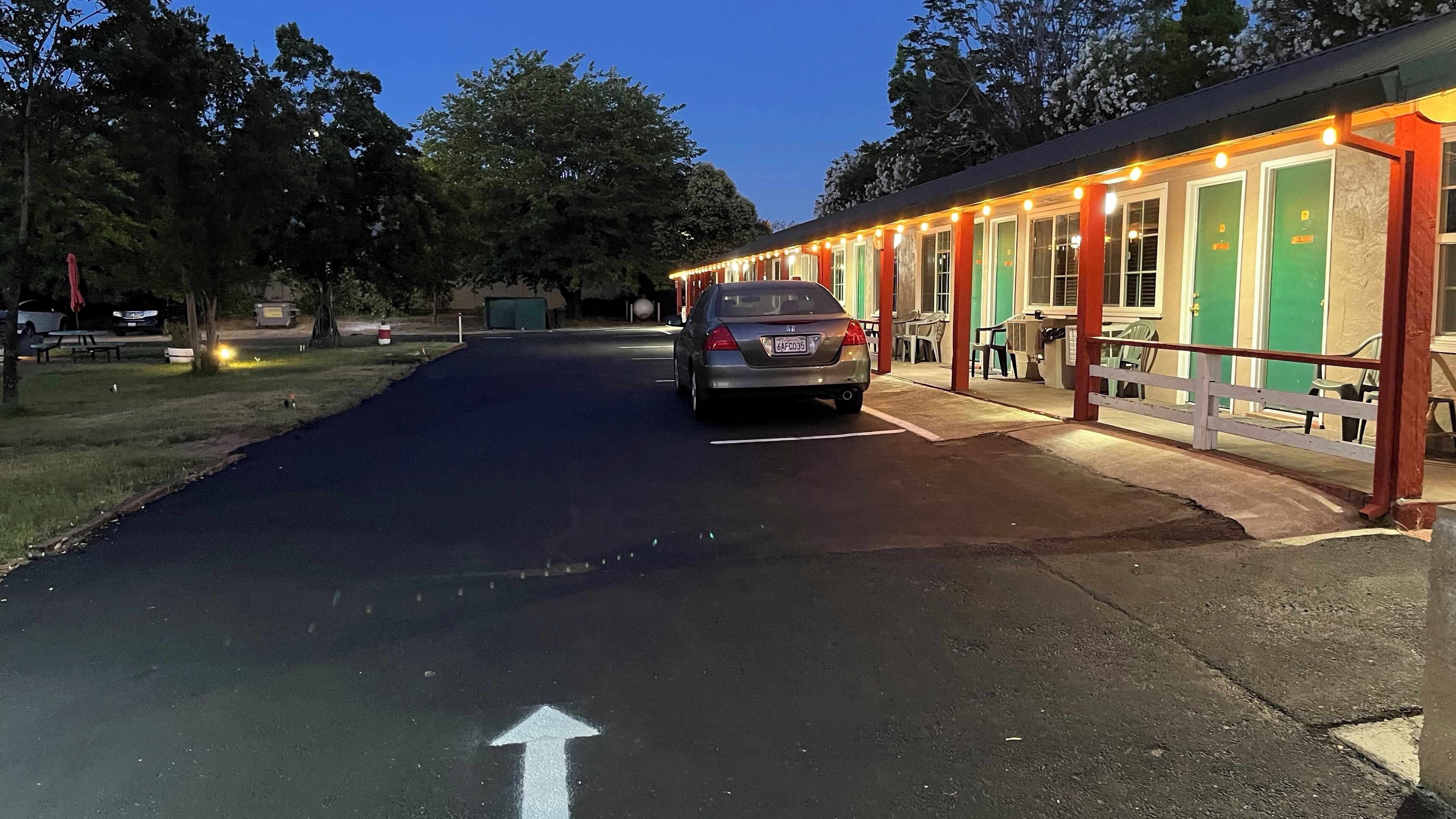 A building with a row of green doors, a parking lot, and a car parked in front.