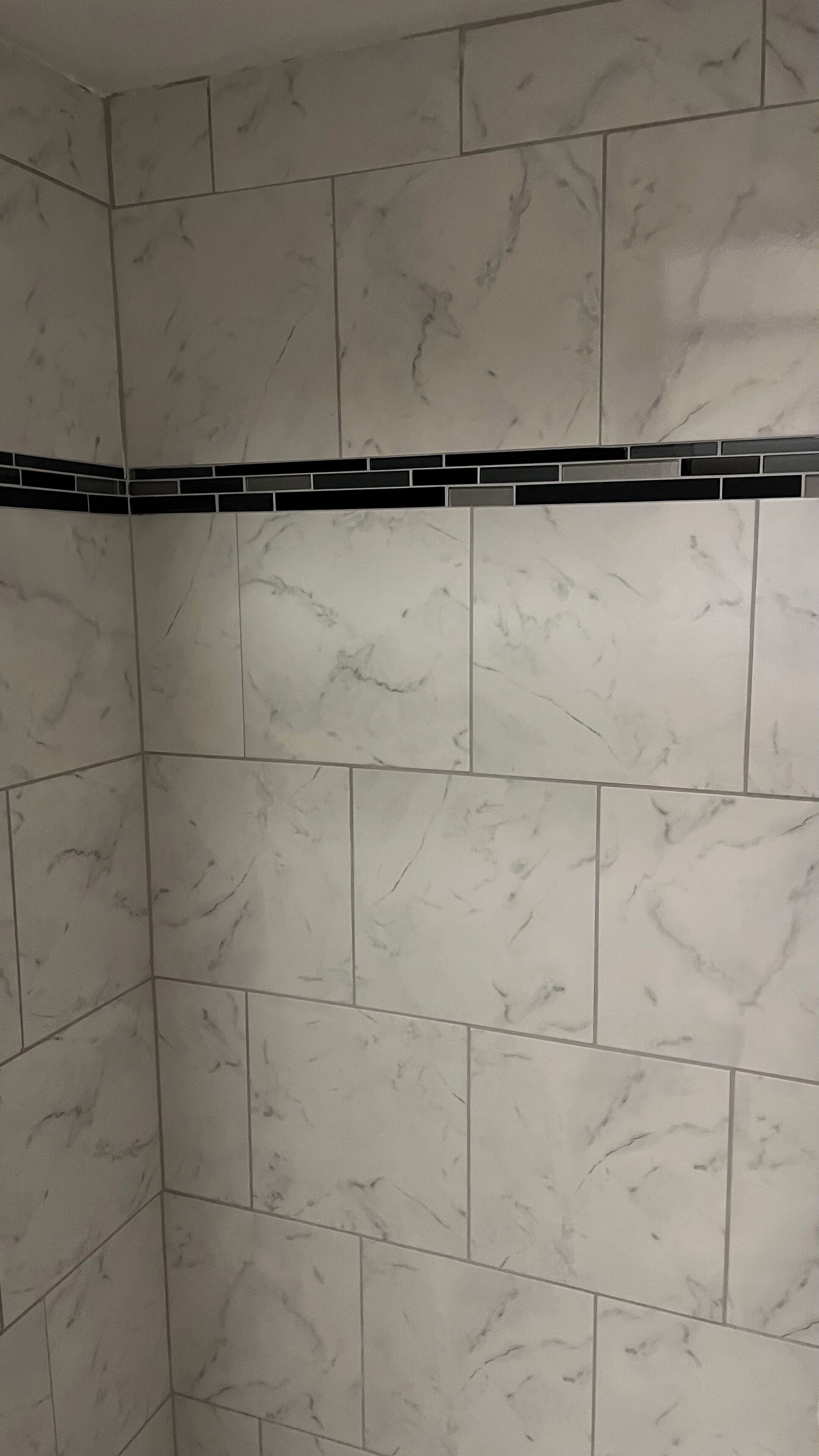 Un área de ducha con azulejos de mármol blanco y un borde de azulejos negros.