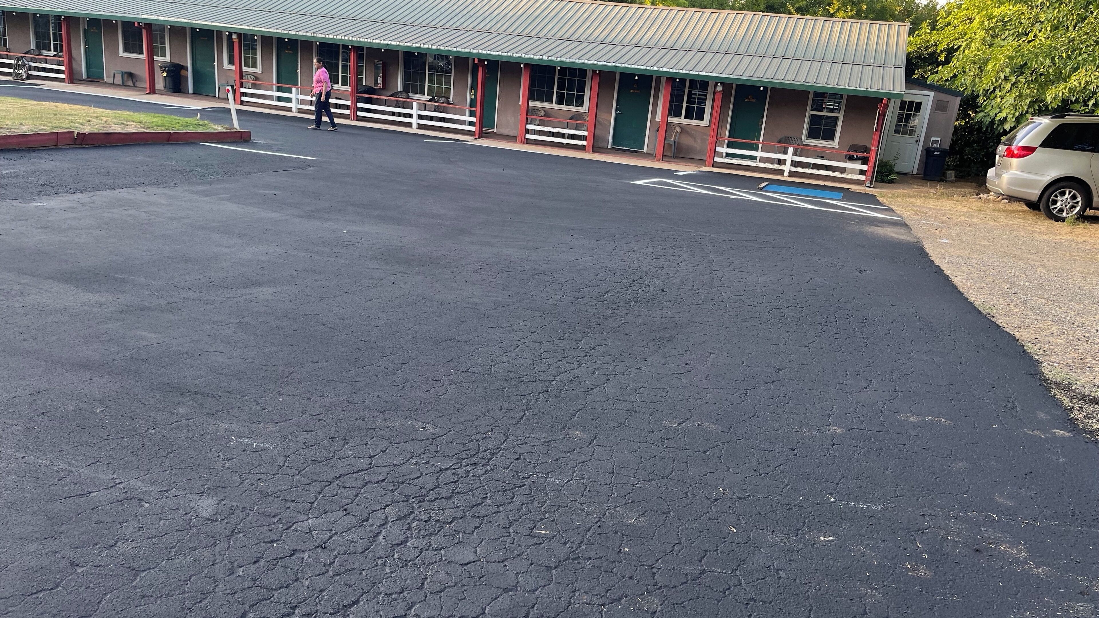 A motel with a large parking lot, a covered outdoor seating area, and a single-story building with a green roof.